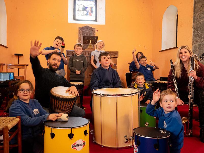 Pupils and professinal artists playing musical instruments in a church and waving, smiling, making funny faces to the camera
